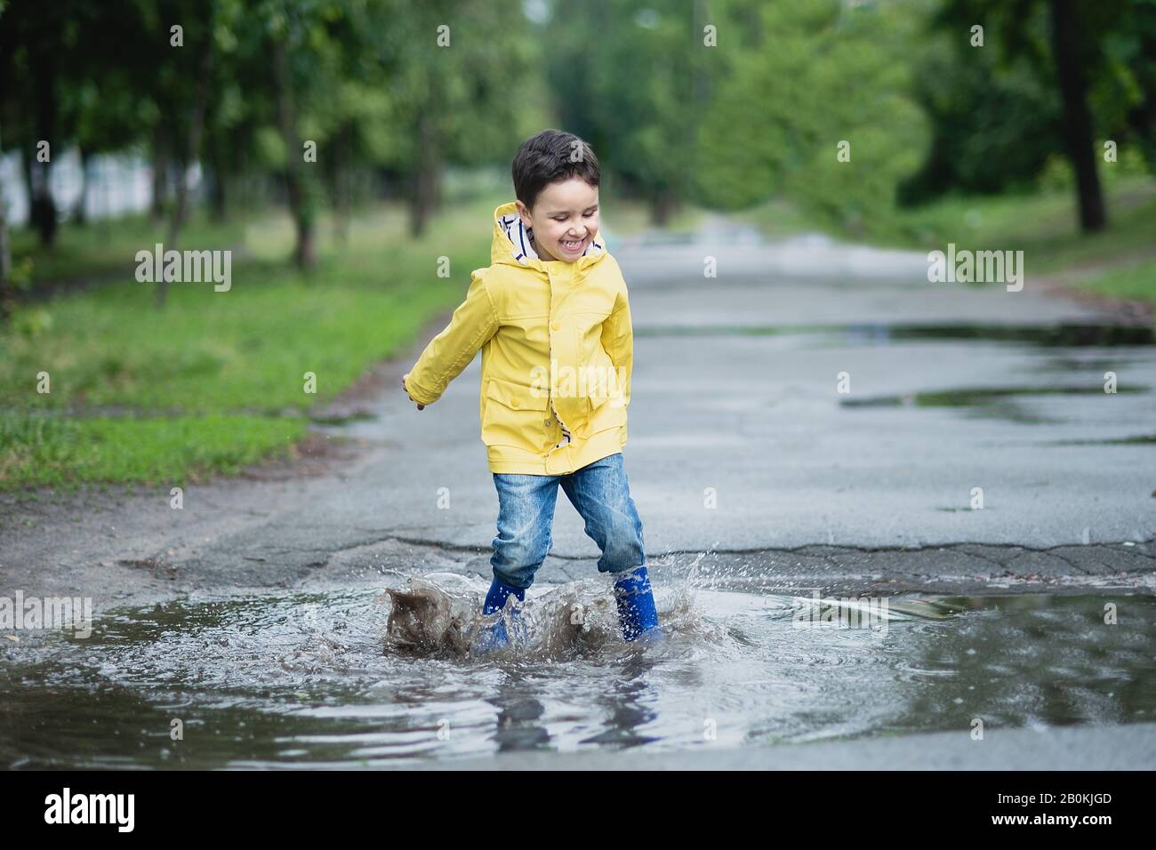 Little boy in raincoat and rubber boots playing in puddle Stock Photo ...
