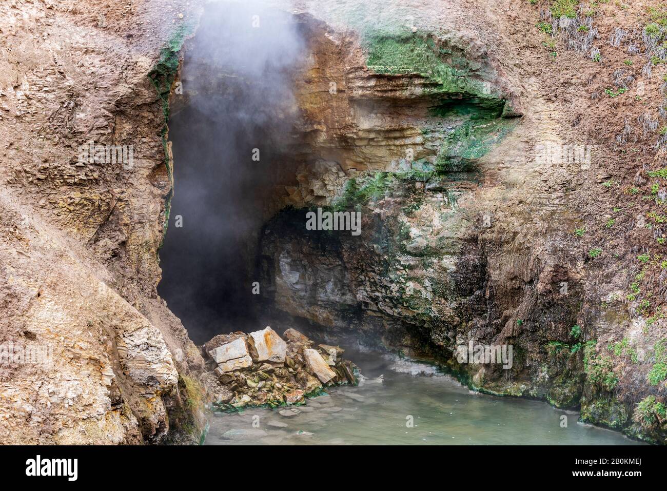 Cave entrance with steam and gas coming out. Hot spring at entrance to cave. Stock Photo