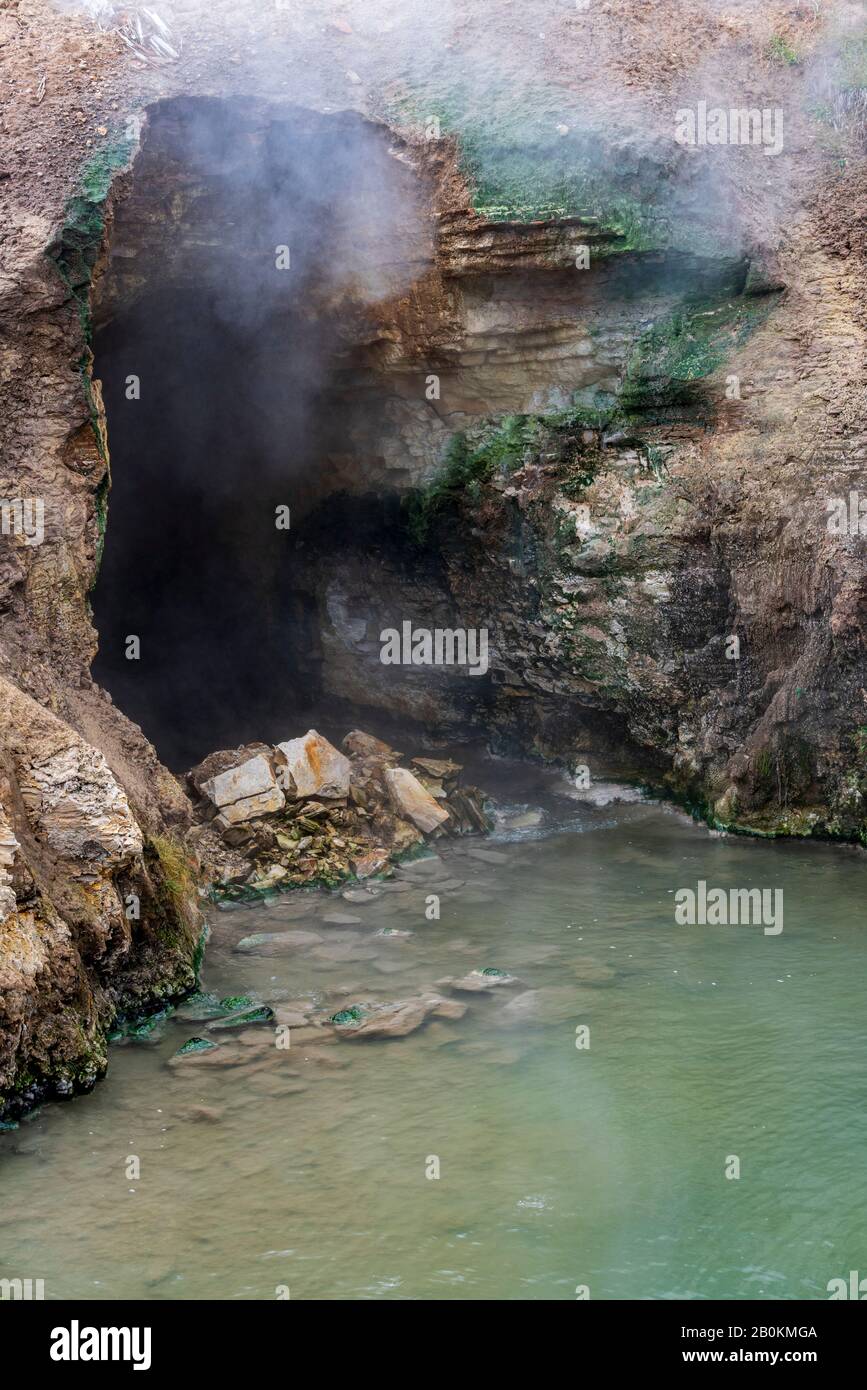 Cave entrance with steam and gas coming out. Hot spring at entrance to cave. Stock Photo