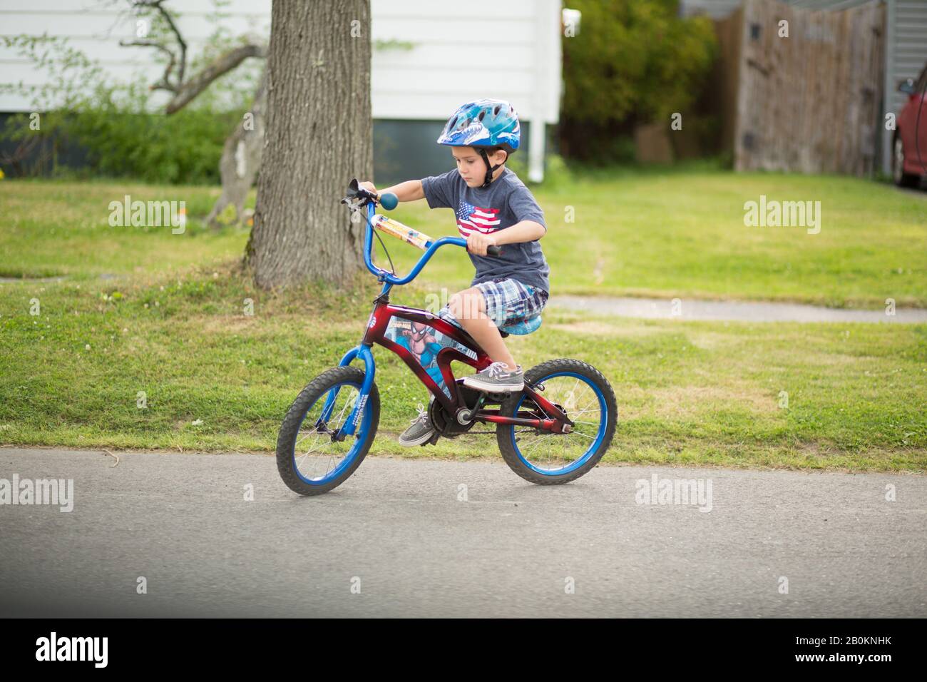 Young American boy riding a bike in the street. He was learning how to ride a bike and wearing a helmet. He is 5 years old and in Portland Maine. Stock Photo