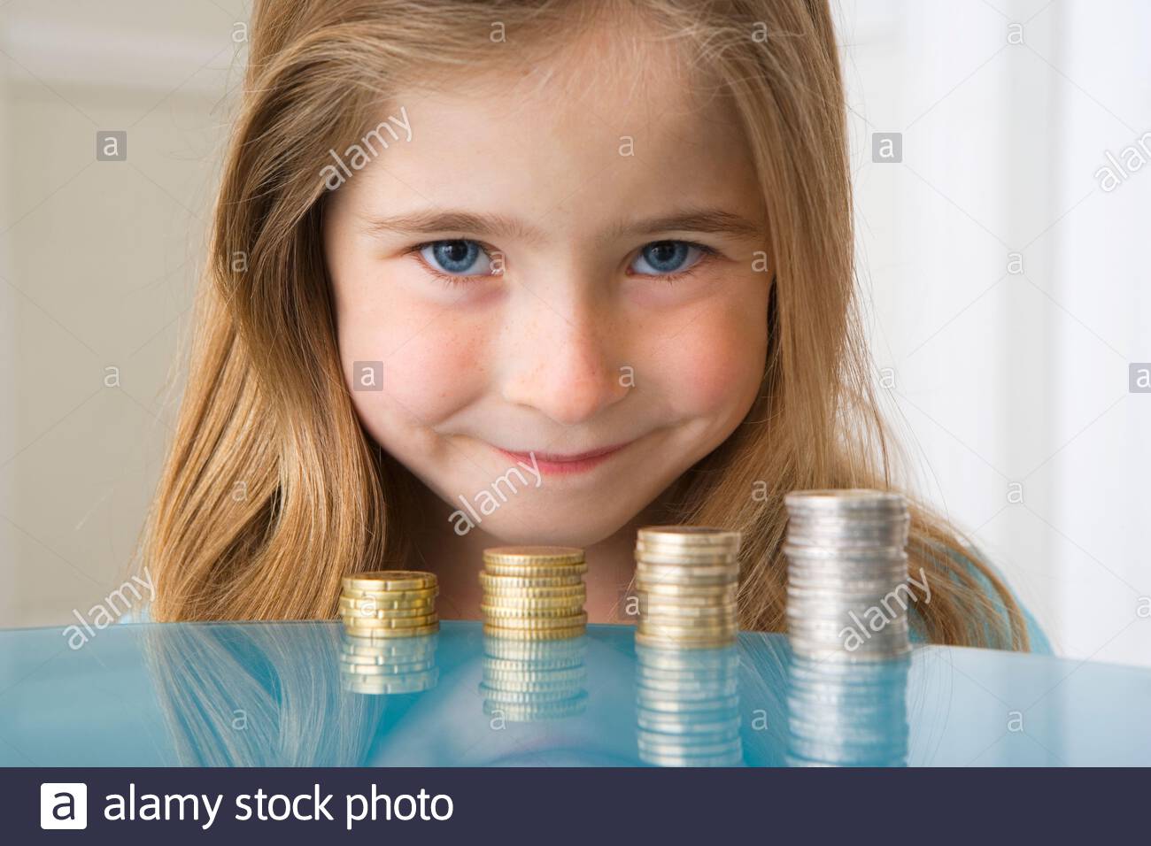 Girl smiling behind coins, careful saver Stock Photo