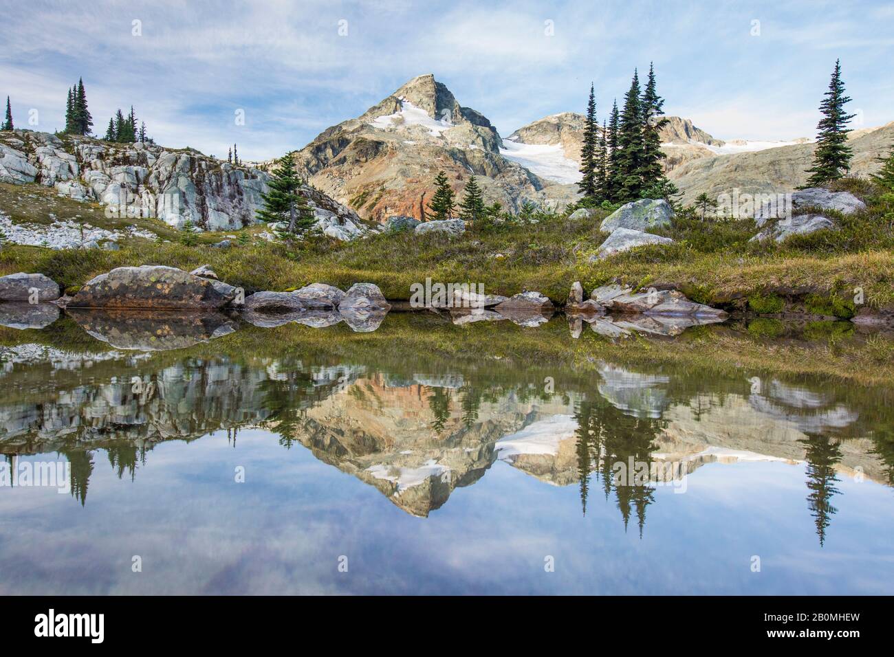 Alpine meadow and mountains reflecting in lake. Stock Photo