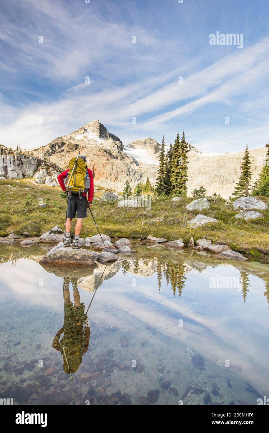 Rear view and reflection of backpacker looking at mountain summit. Stock Photo