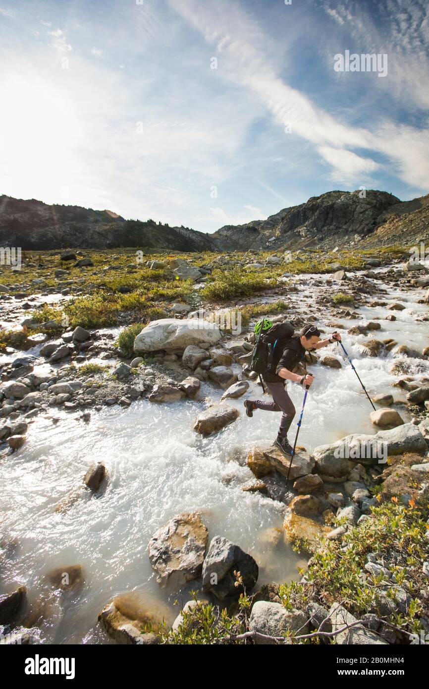 Backpacker uses boulders to cross mountain creek. Stock Photo