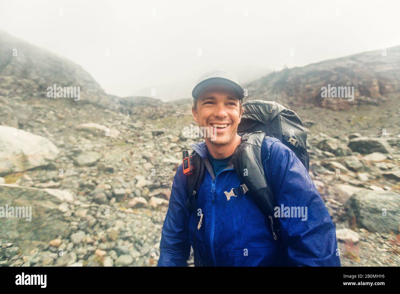 Backpacker smiling despite bad weather, rain and wind. Stock Photo
