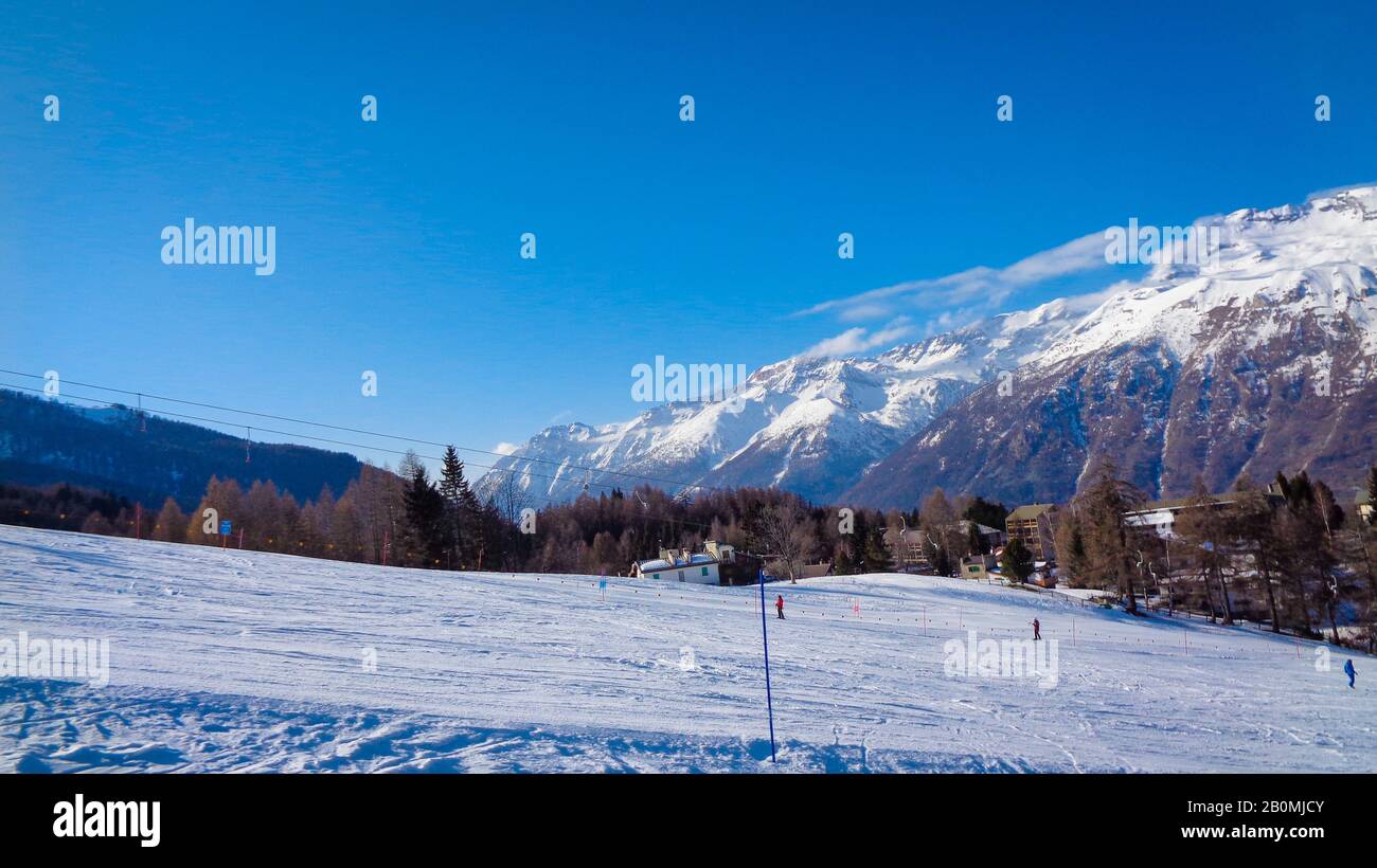 Mountain landscape with winter snow and people enjoy skiing under blue sky, Italy Stock Photo