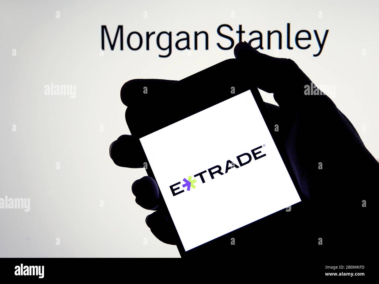 E-trade logo on a smartphone in a hand with Morgan Stanley on the blurred background. Concept for company acquisition. Real photo, not a montage. Stock Photo