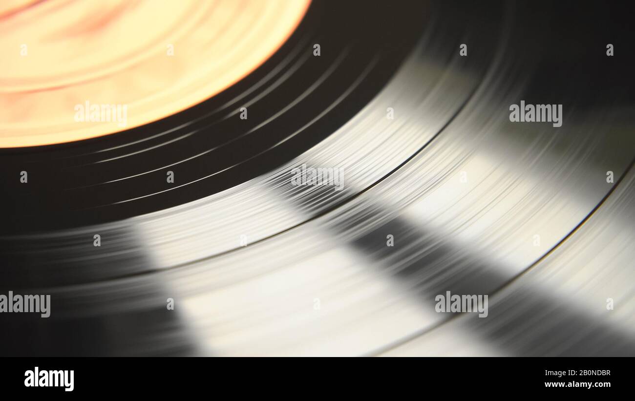 An abstract view of the rotating motion of a black vinyl disc. Daytime natural light reflections on the soundtrack surface. Top view scene. Stock Photo