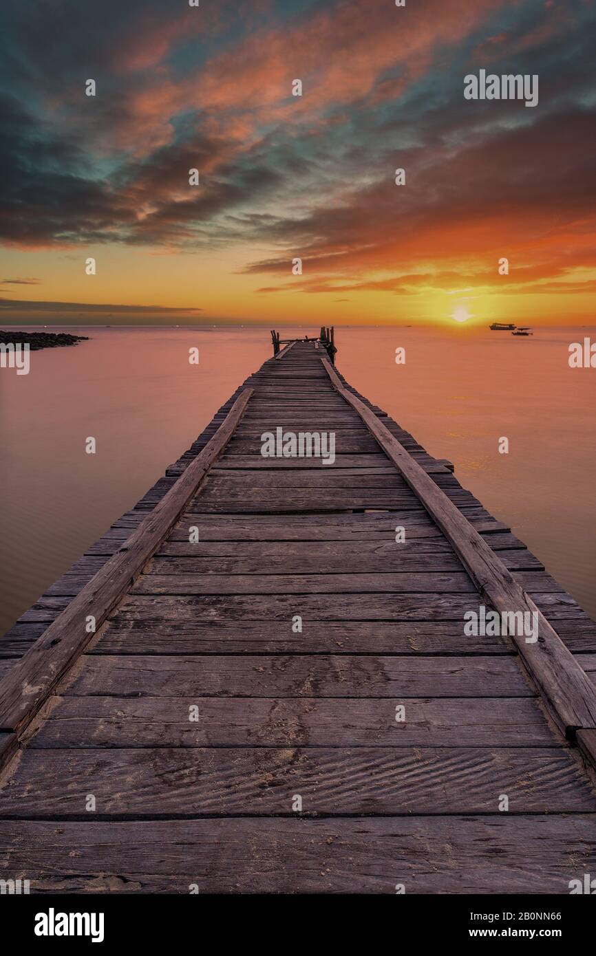 Old wooden pier stretching out into the sea with a dramatic sunset ...