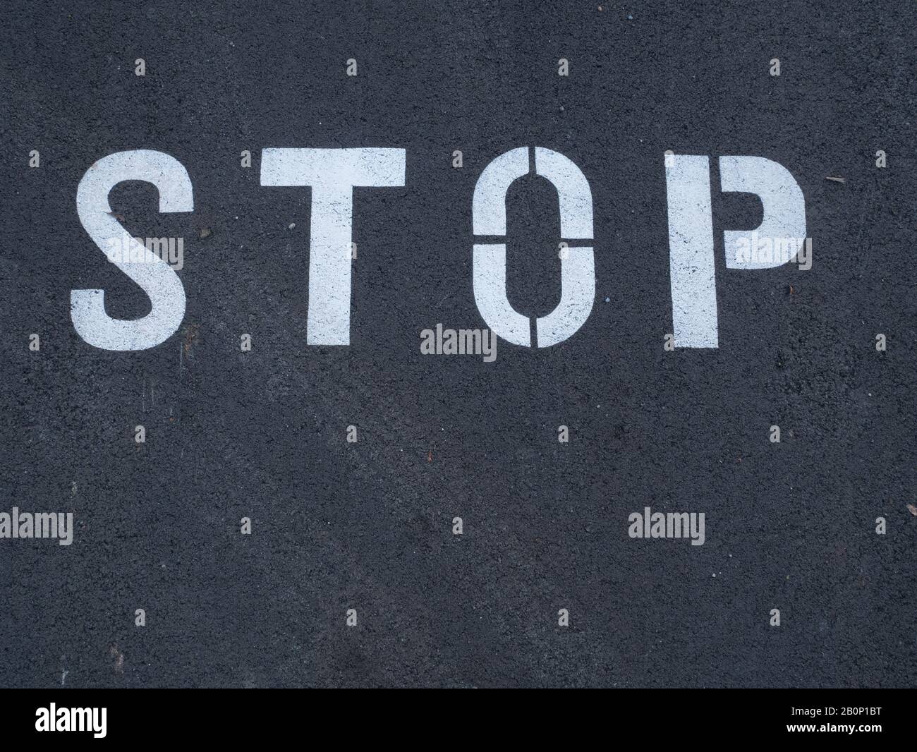 White stop sign painted on dark asphalt. You can see tire tracks over it. Indicates a mandatory stop. Stock Photo