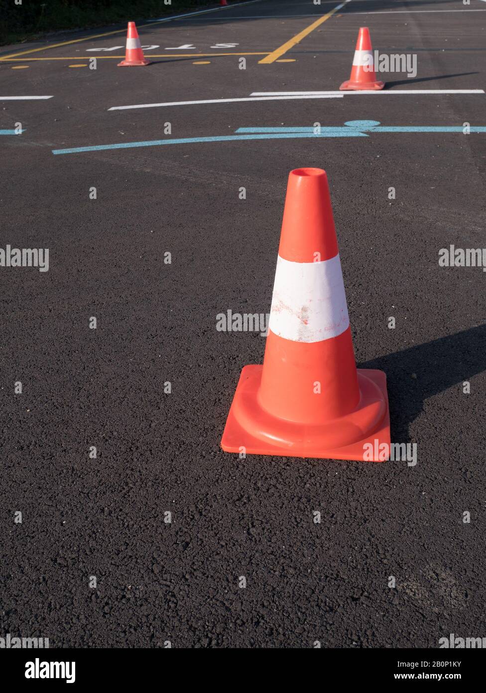 Traffic cone with shadow on asphalt. Traffic cone, with white and orange stripes on gray asphalt, copy space. Stock Photo