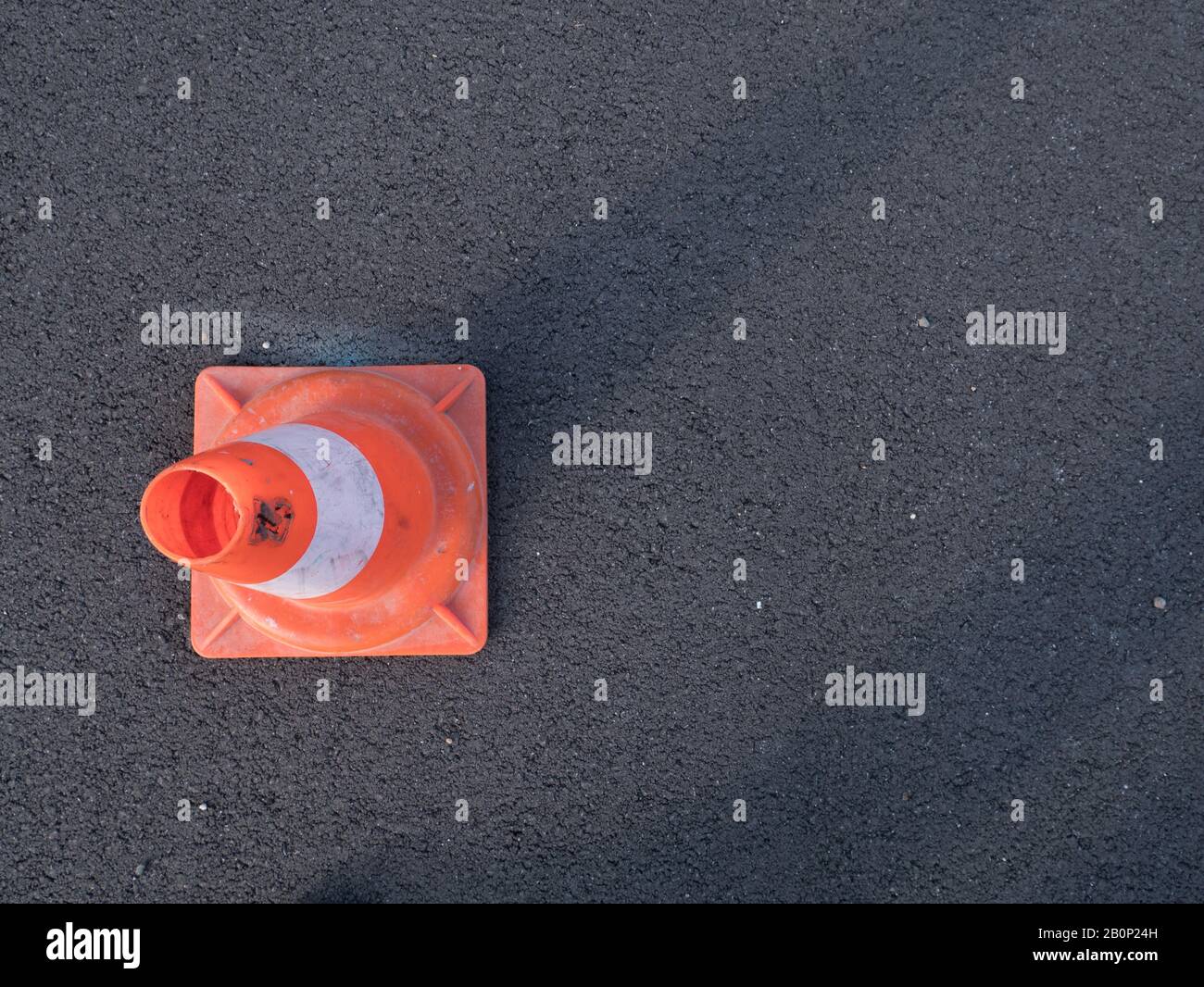 Traffic cone with shadow on asphalt. Traffic cone, with white and orange stripes on gray asphalt, copy space. Stock Photo
