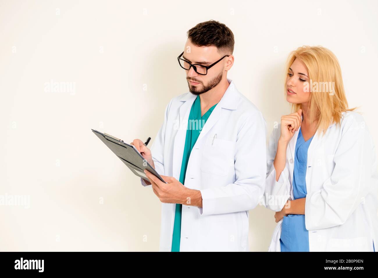 GP doctor looks at data in documents on clipboard while discussing with