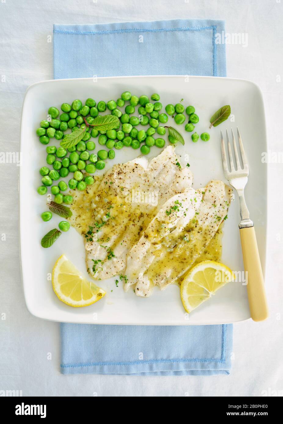 Wild pacific poached sole fillets drizzled with lemon butter sauce and organic minty peas.  White plate in flat lay composition and shot in natural li Stock Photo