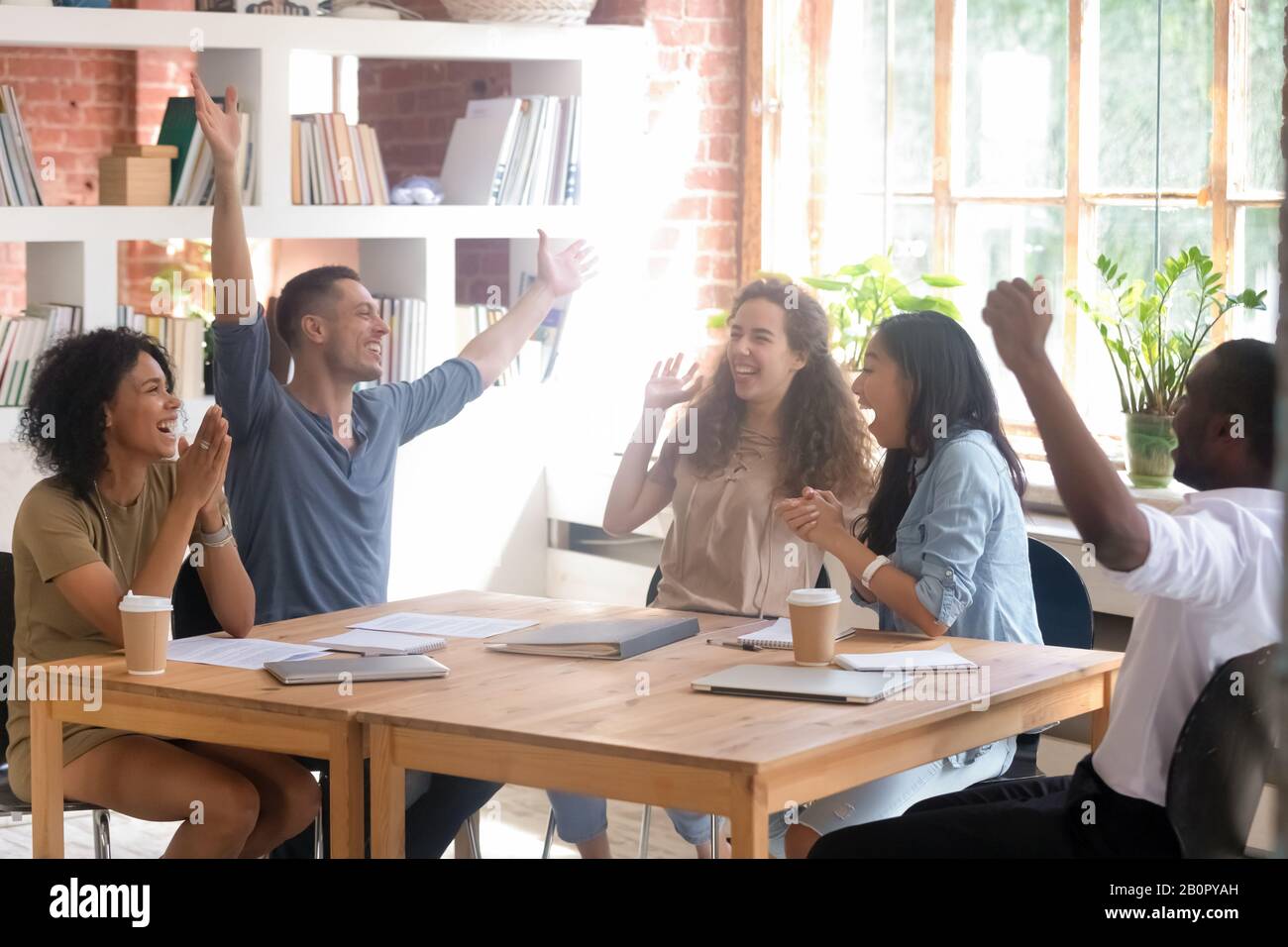 Excited diverse students or employees celebrating success, business achievement, good exam result at meeting, happy African American and Asian team me Stock Photo