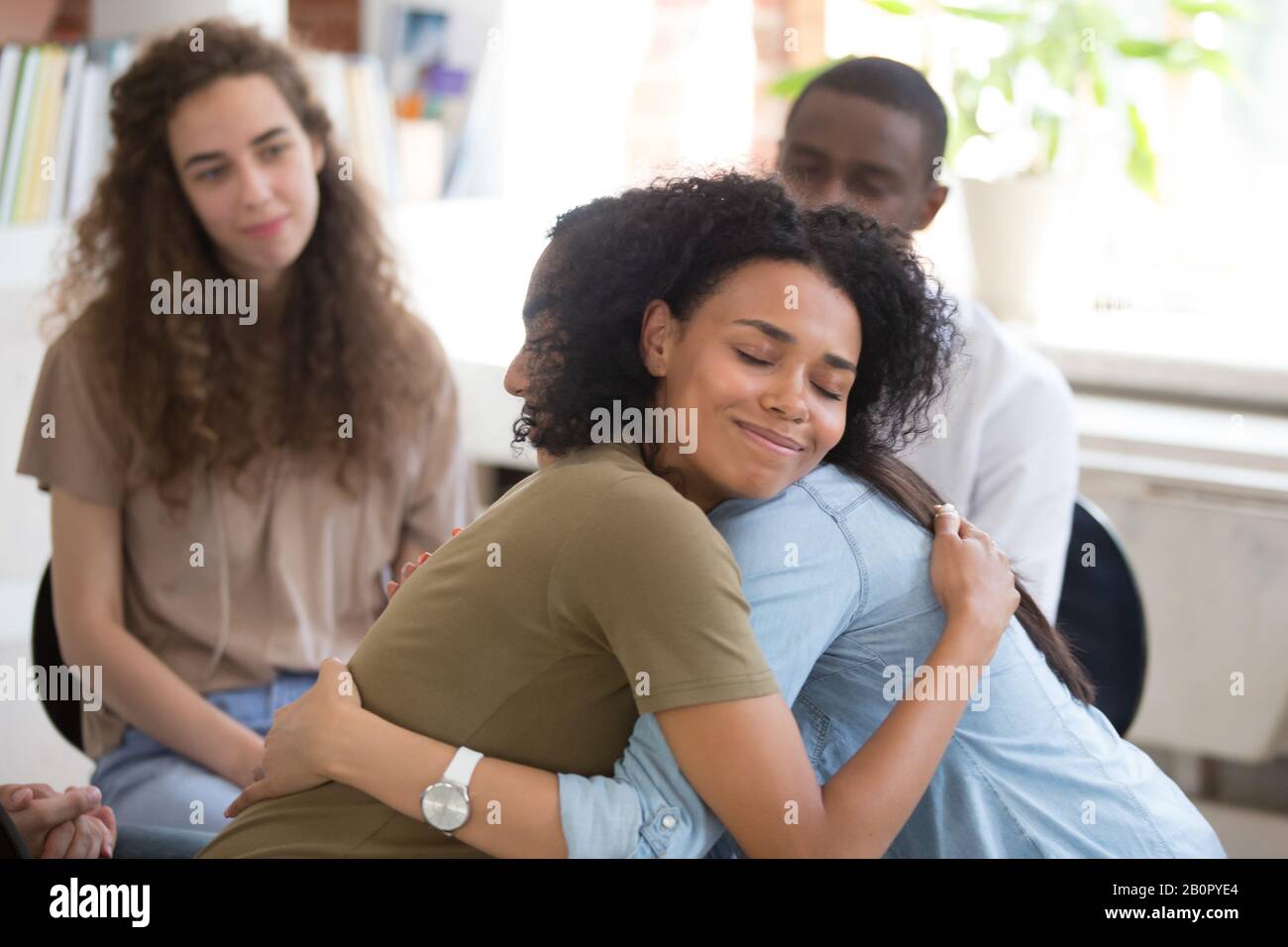 African American and Asian women embracing at group therapy session, empathy concept, psychological support, diverse friends overcome problem together Stock Photo