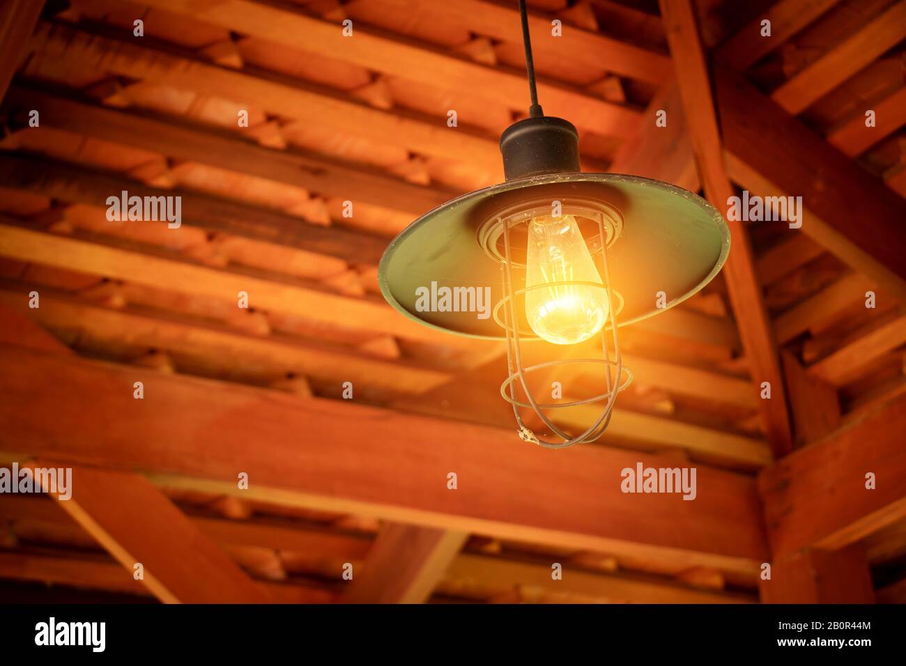 Incandescent light bulb hanging from ceiling over head from roof house gable corner at Asian countryside. Incandescent light bulb, old style and low t Stock Photo