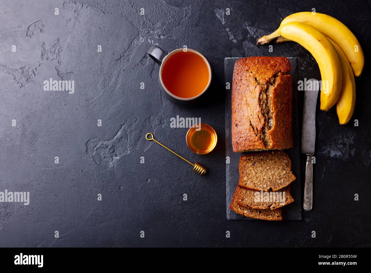 Banana, coconut bread, cake with cup of tea on slate board. Dark stone background. Copy space. Top view. Stock Photo