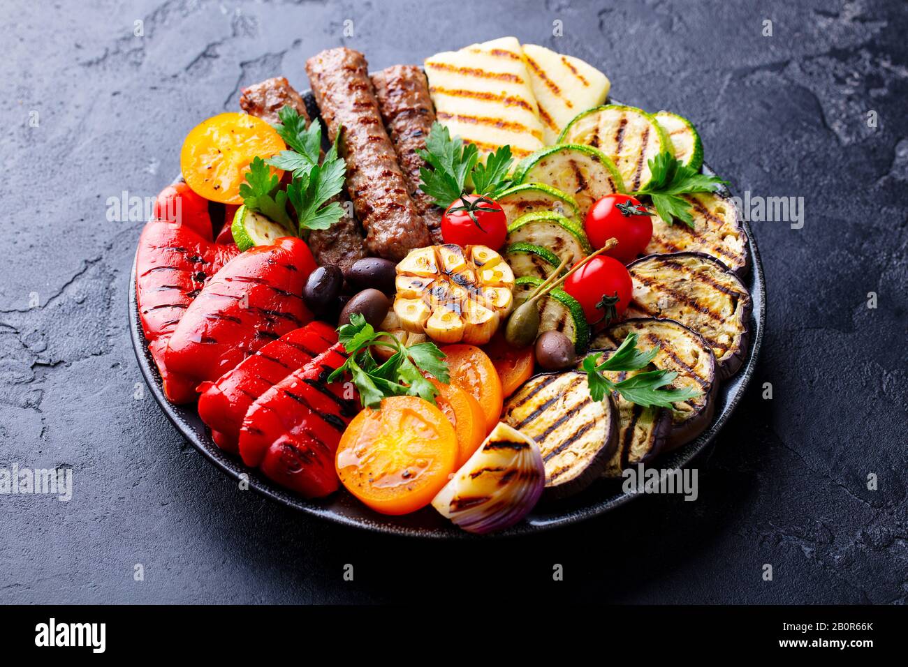 Grilled meat kebabs and vegetables on a plate. Black stone background