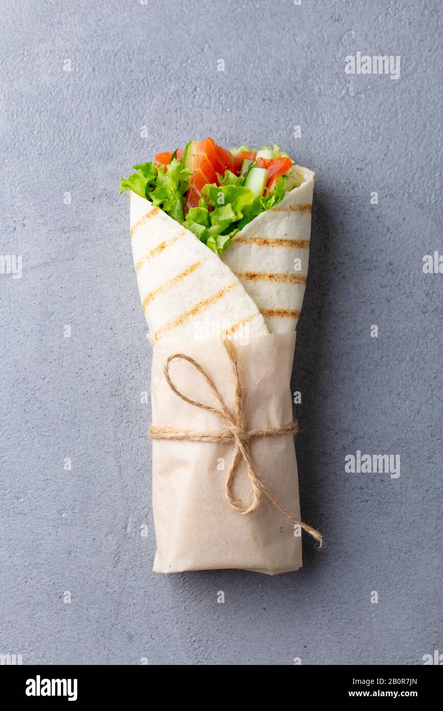 Wrap sandwich, roll with fish salmon and vegetables. Grey background. Top view. Stock Photo