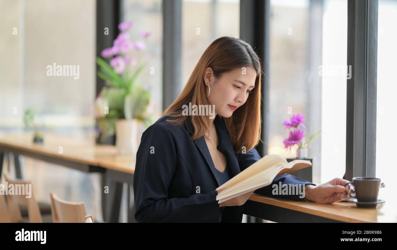 Cropped shot of a woman reading book while sitting on bar stool next window in coffee shop Stock Photo