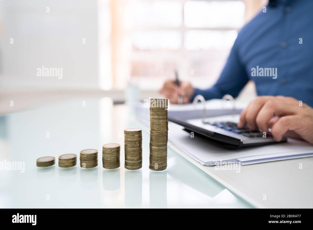 Midsection Of Businessman Calculating Invoice With Stacked Coins Arranged At Office Desk Stock Photo