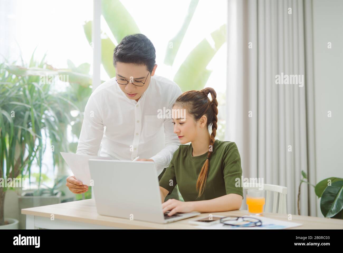 Wide shot of smiling couple surfing in laptop sitting at table Stock Photo