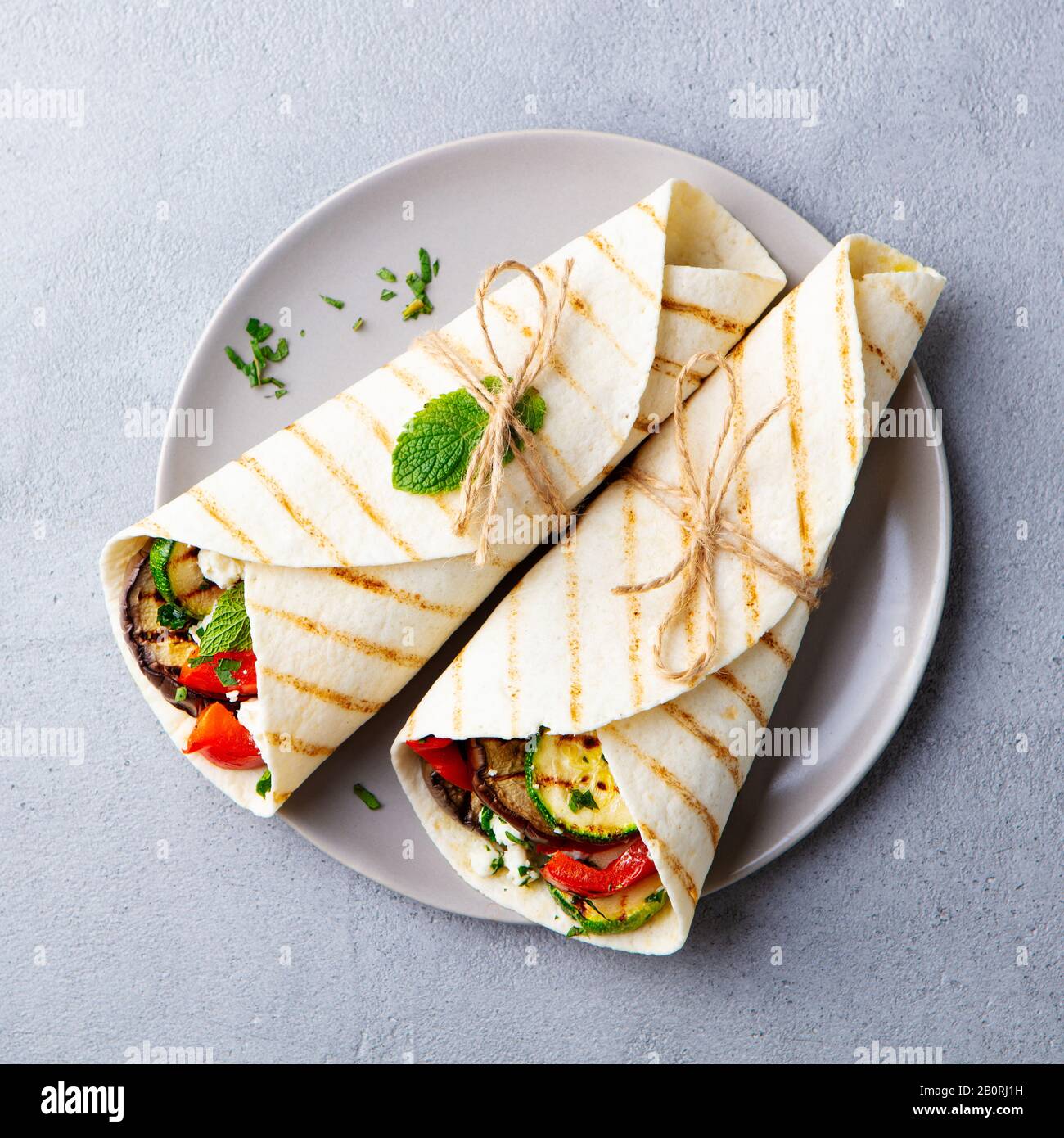 Wrap sandwich with grilled vegetables and feta cheese on a plate. Grey background. Top view