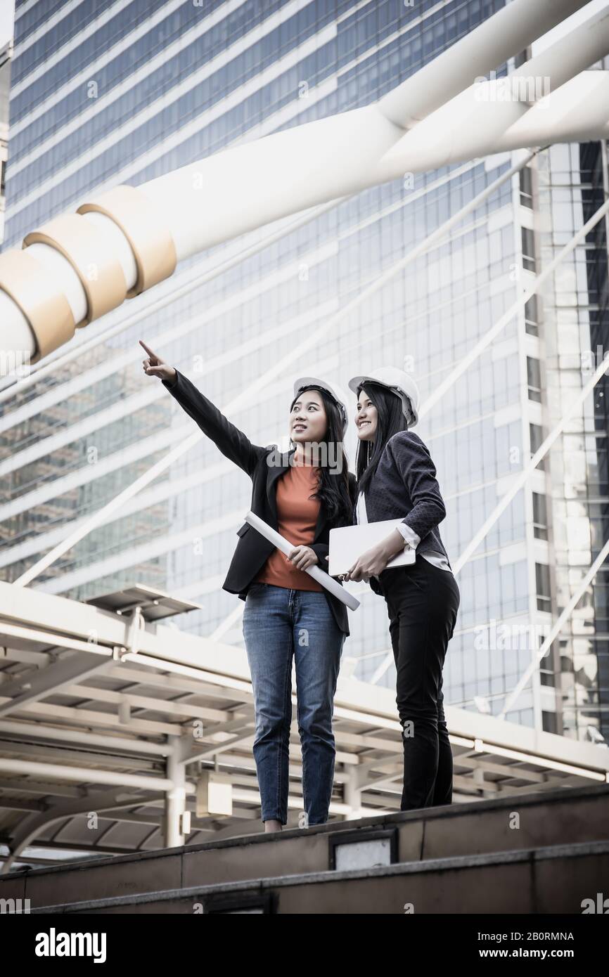Two Young architects looking at blueprint in front of construction site building. Stock Photo