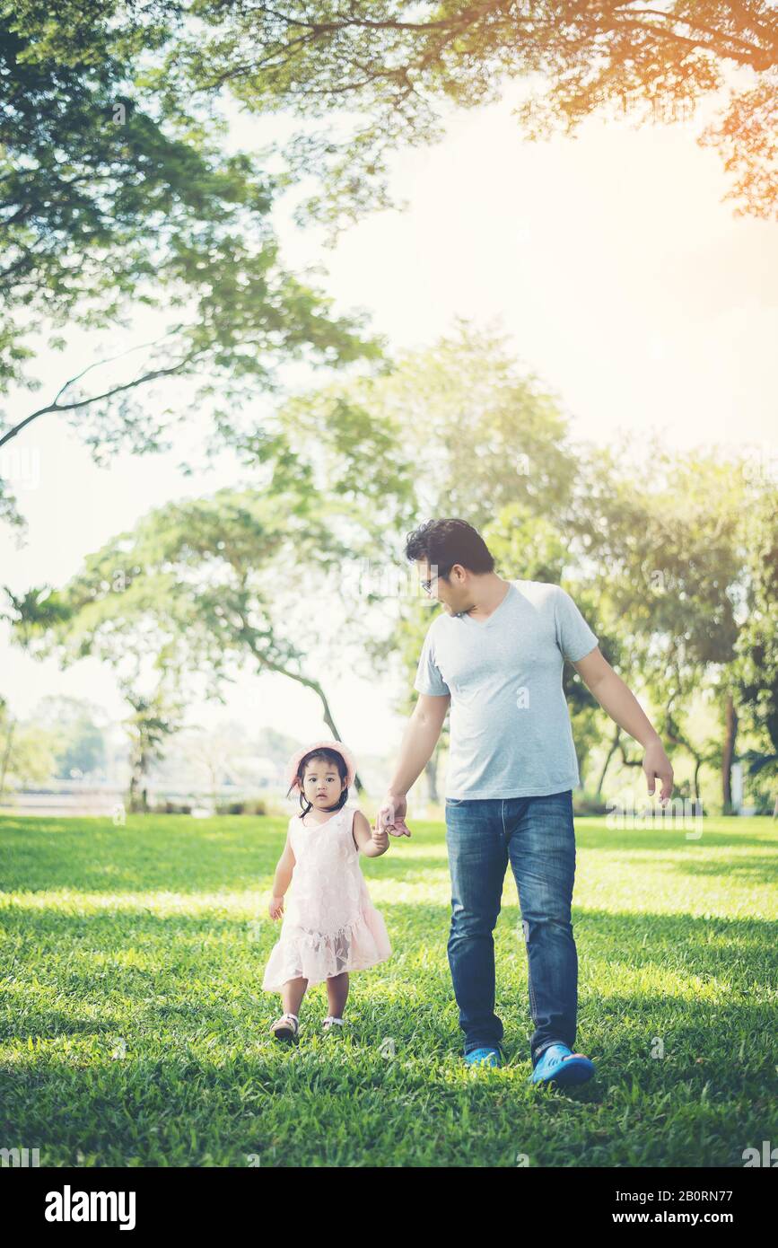 Toddler girl holding hands with her father walking in the park ...