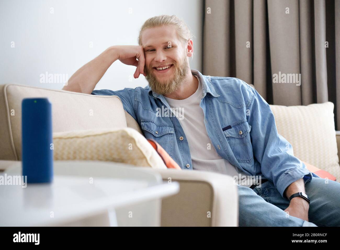 Smiling man relax on sofa look at camera use portable wireless speaker on table Stock Photo