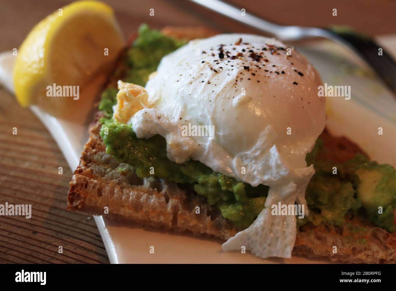 Poached egg with pepper on guacamole with toast and a wedge of lemon Stock Photo