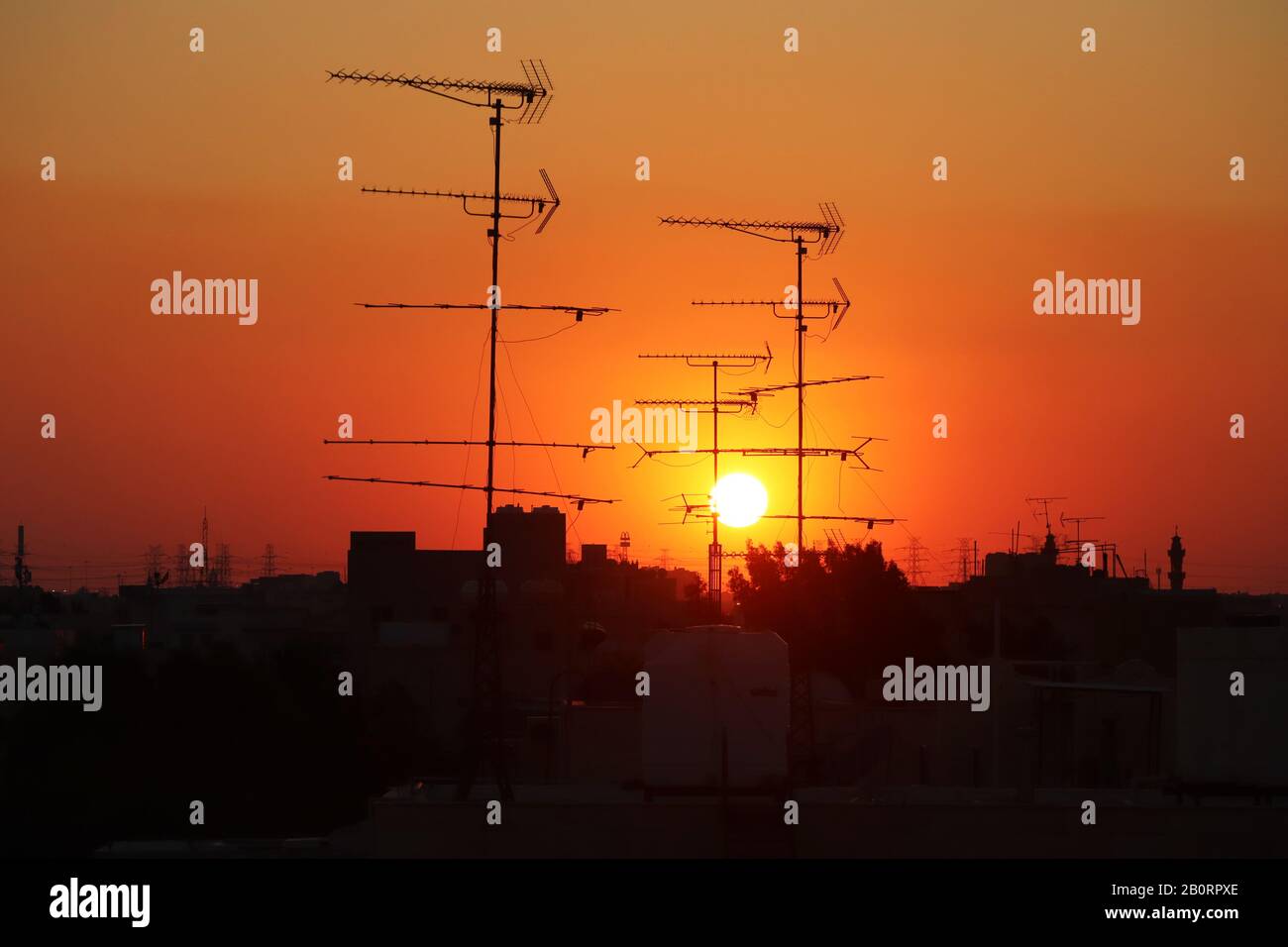 Analogue television reception antennas on a rooftop silhouetted against a setting sun Stock Photo