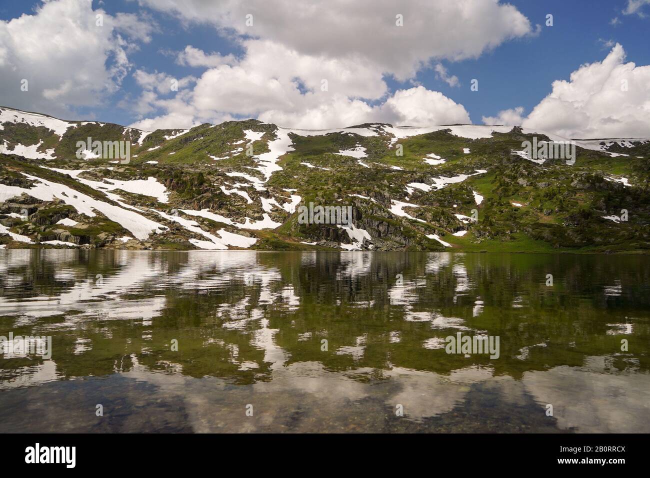 Small mountain lake surrounded with mountain slopes covered with little