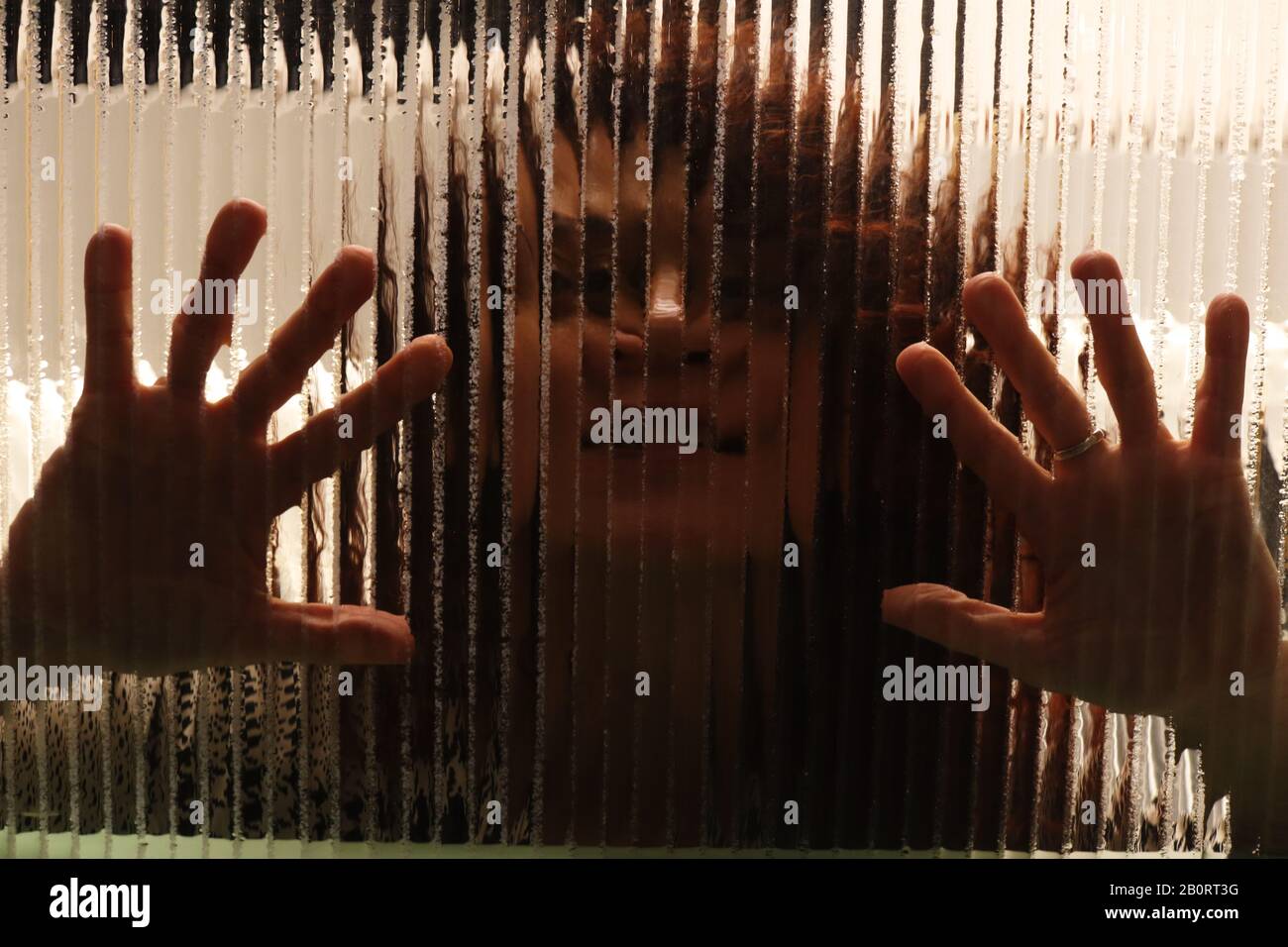 Creepy scary image of girl behind glass with palms of hands on textured glass Stock Photo