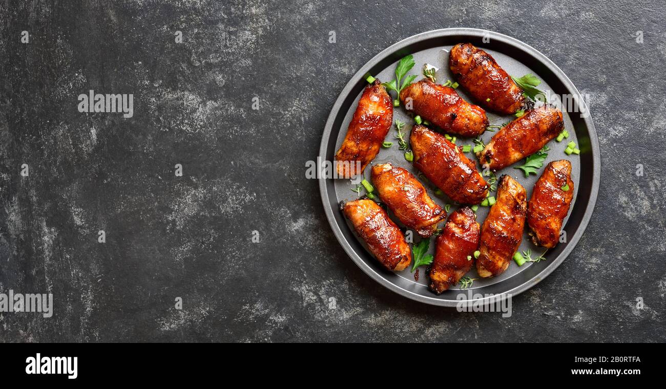 Bacon wrapped grilled chicken wings on plate over black stone