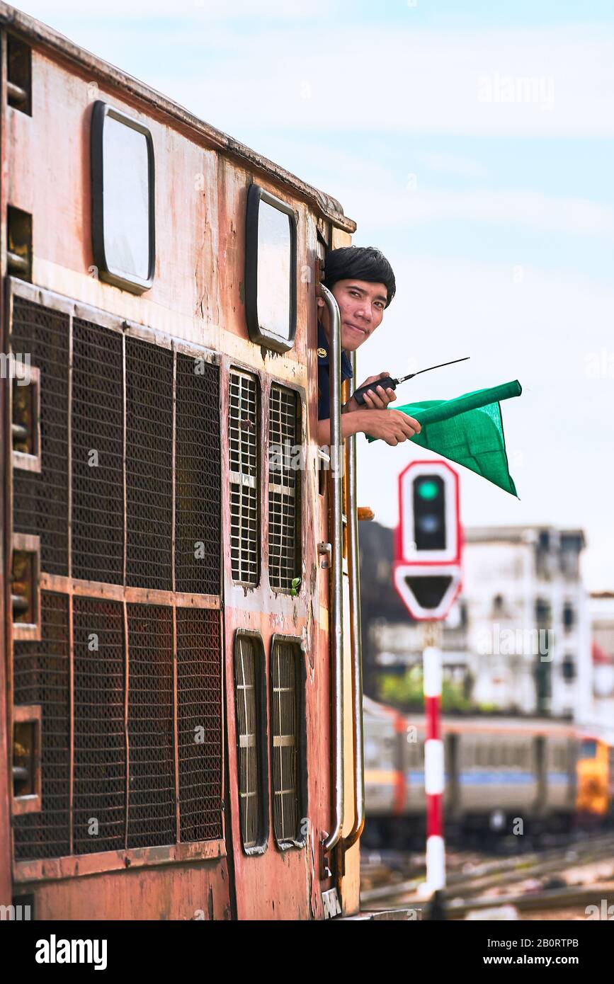 Bangkok, Thailand: Young male railway train driver with green flag and radio got the green light to leave Hualamphong Train Station Stock Photo