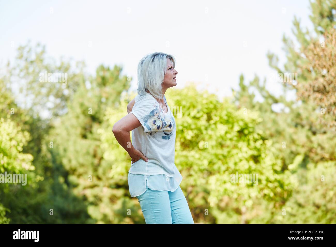Old woman in nature has back pain and is holding her back Stock Photo ...