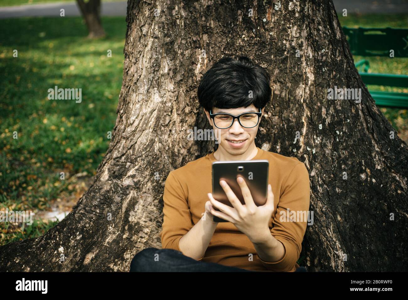 young man using a tablet and sitting under the tree Stock Photo
