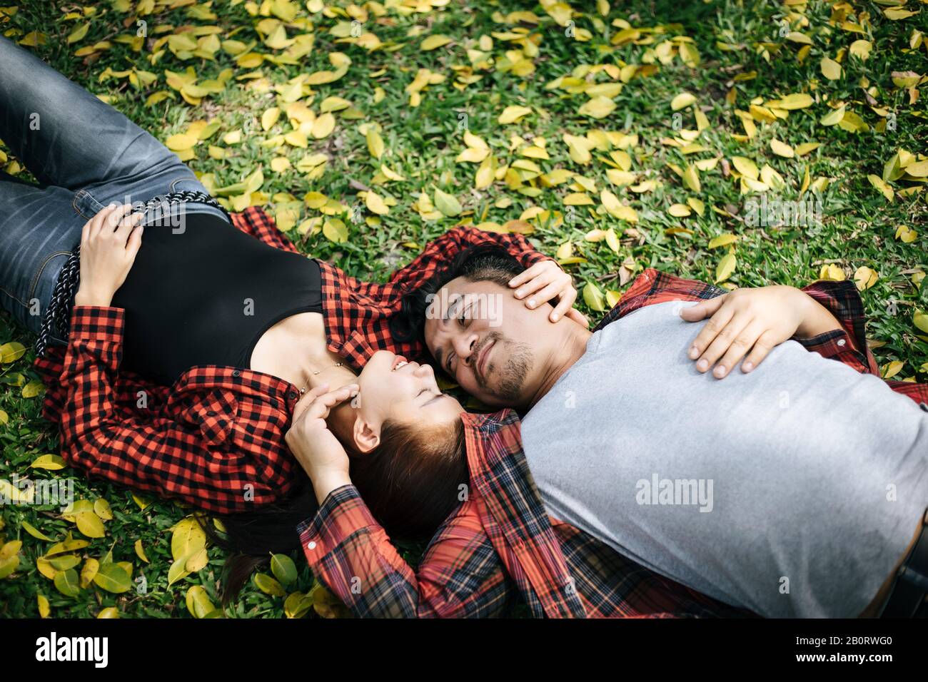 Romantic couple of young people lying on grass in park Stock Photo - Alamy