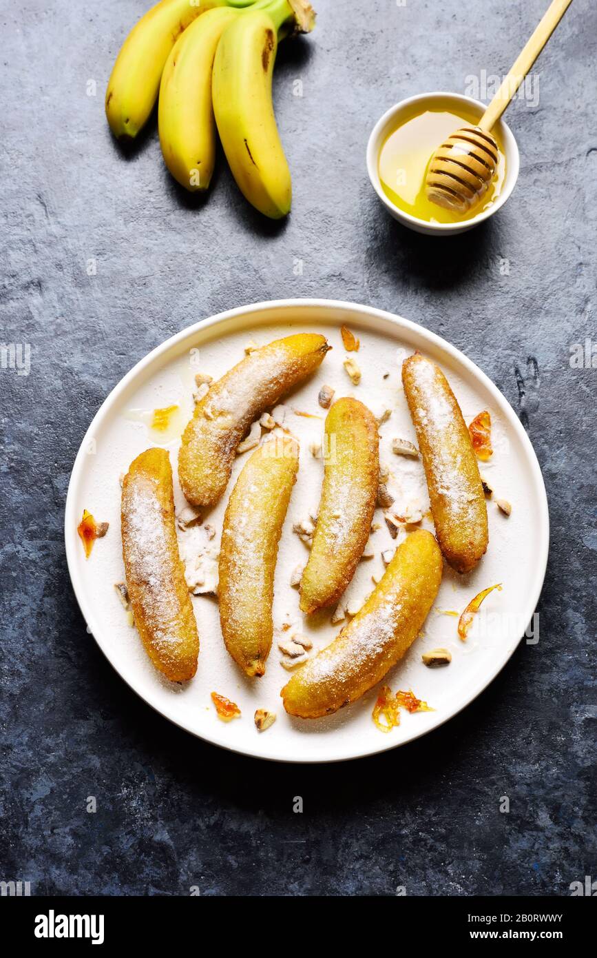 Deep fried bananas on white plate over blue stone background. Tasty