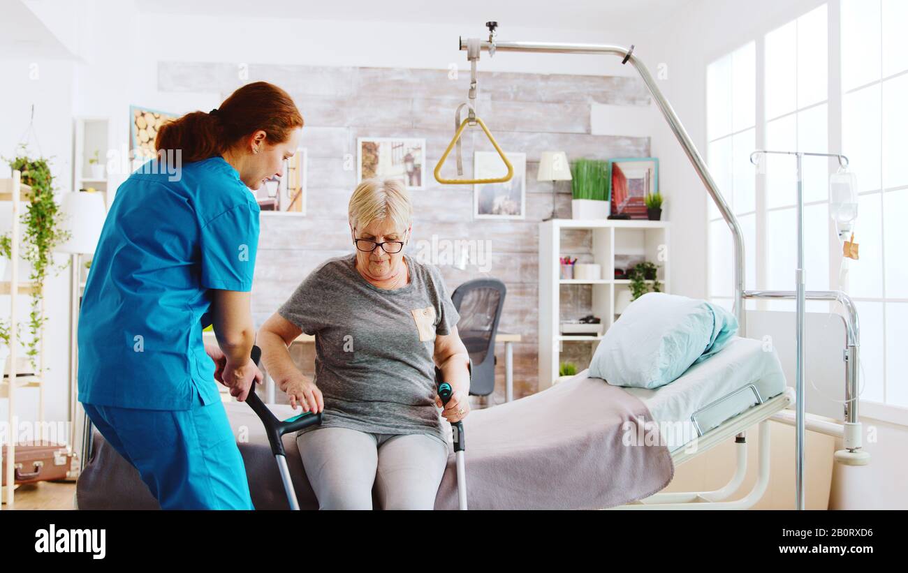 Old disabled lady walking with the help of crutches in nursing home