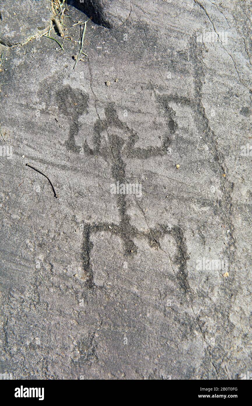 Petroglyph, rock carving, of a schematic human figure in a 'prayer' position wearing a crested helmet. Carved by the ancient Camuni people in the iron Stock Photo