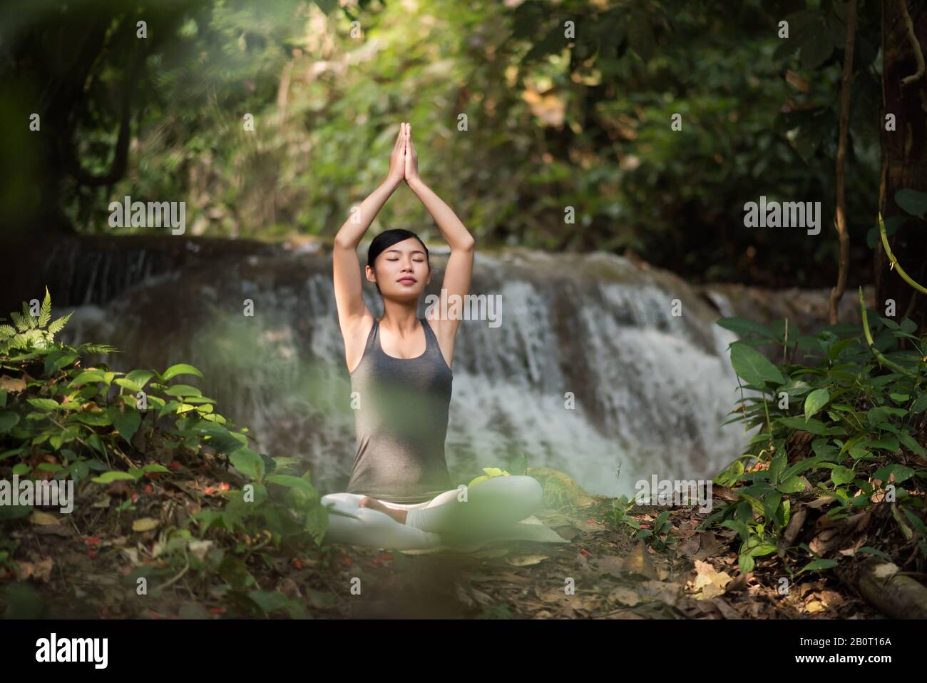 Young woman in yoga pose sitting near waterfall Stock Photo - Alamy