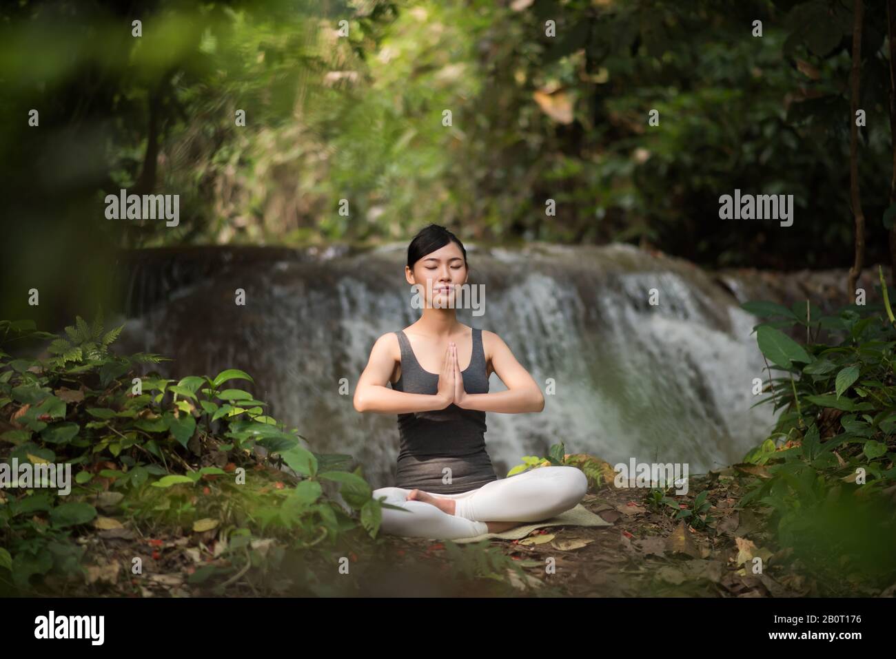 Young woman in yoga pose sitting near waterfall Stock Photo - Alamy