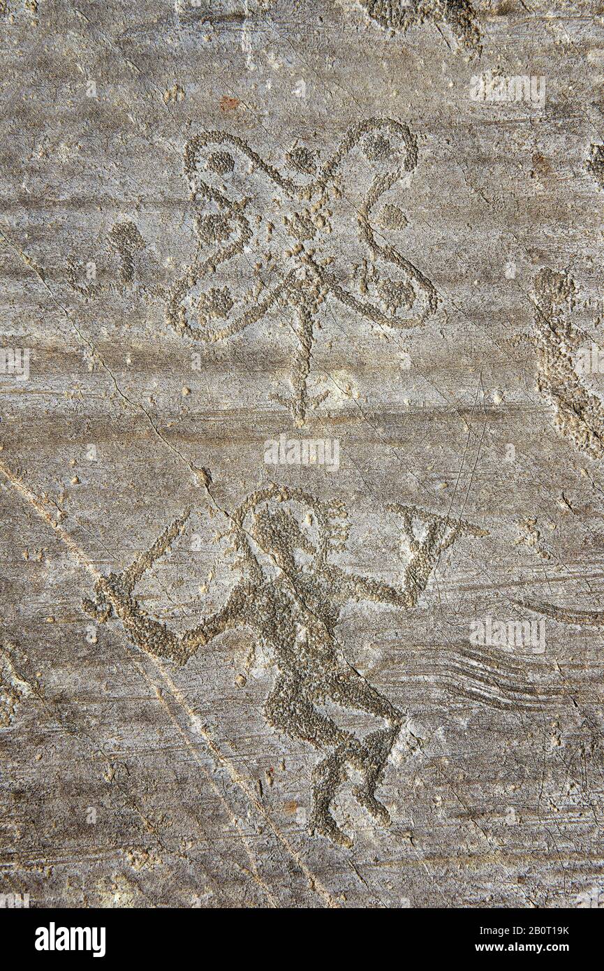 Petroglyph, rock carving, of a warrior  carrying with a sword and a round shield and wearing a halo helmet dancing around the so called Camunian Rose. Stock Photo