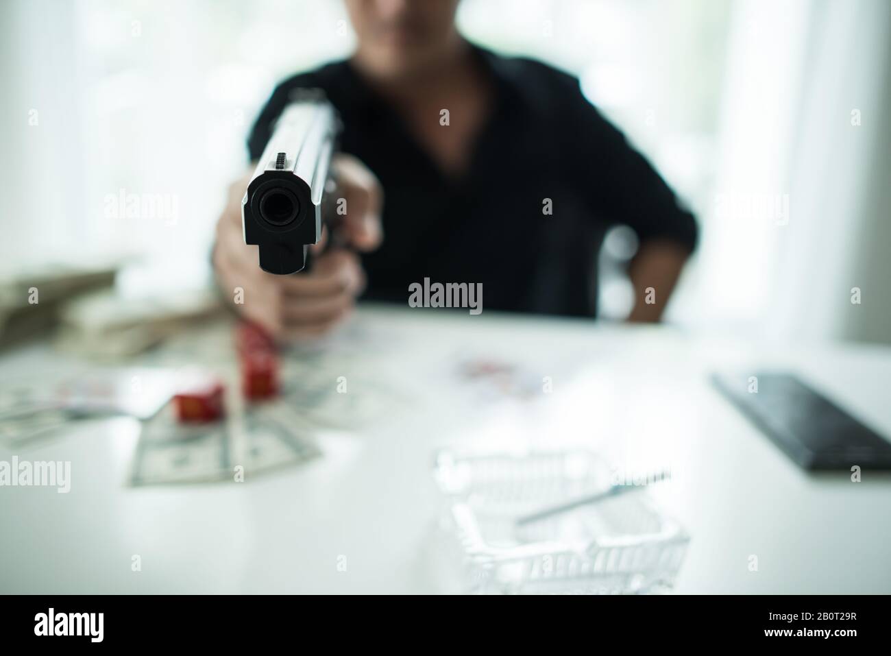 young man sitting on a table holding a gun, have alcohol glass and money on the table. Stock Photo