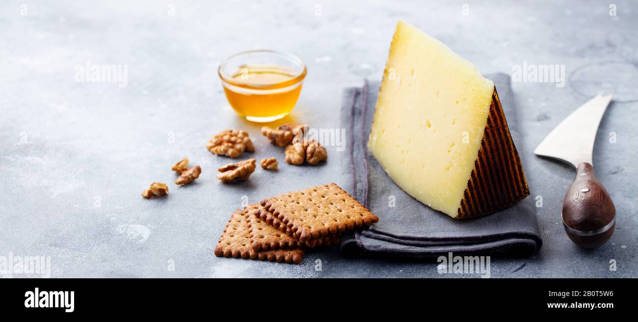 Hard cheese, Manchego with nuts, honey and crackers on grey background. Copy space. Stock Photo