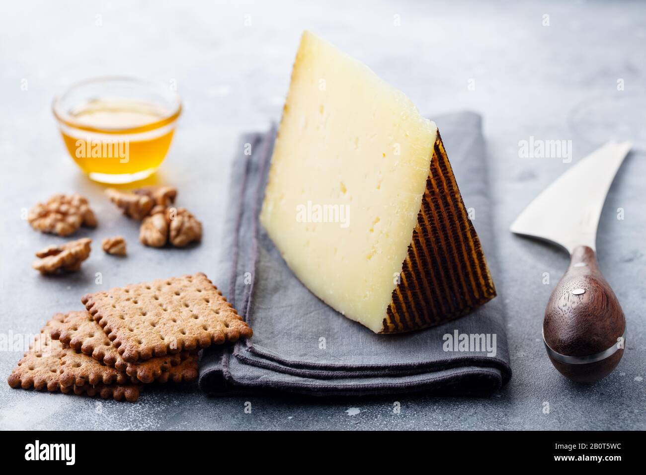 Hard cheese, Manchego with nuts, honey and crackers on grey background. Close up. Stock Photo