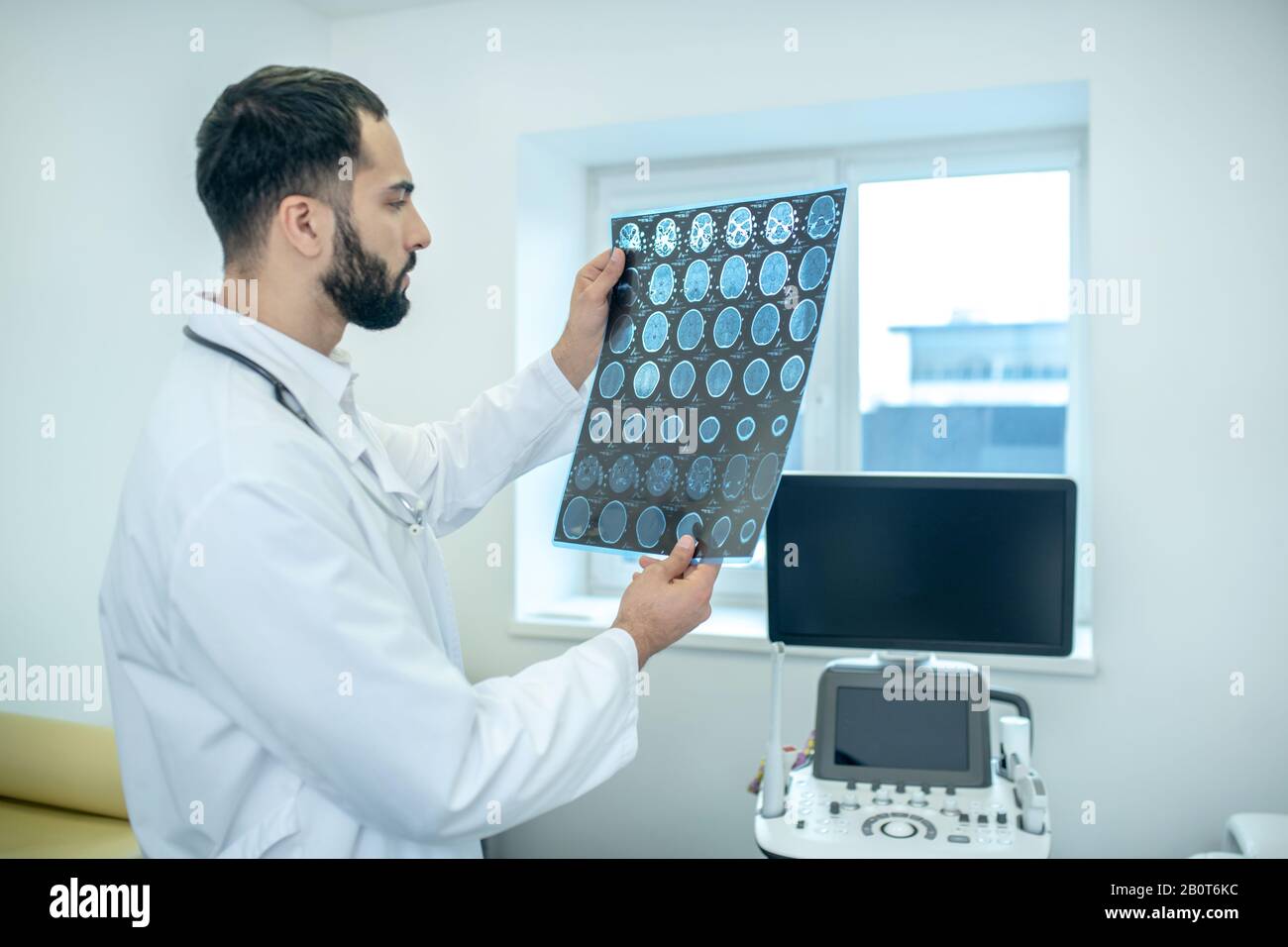 Male bearded doctor in a white robe analyzing MRI results looking concentrated Stock Photo